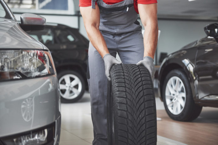 Closeup of mechanic hands pushing a black tire in the workshop